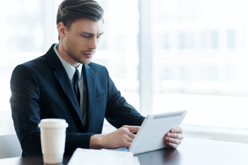 Internet user. Cheerful young man using digital tablet while coffee break in office